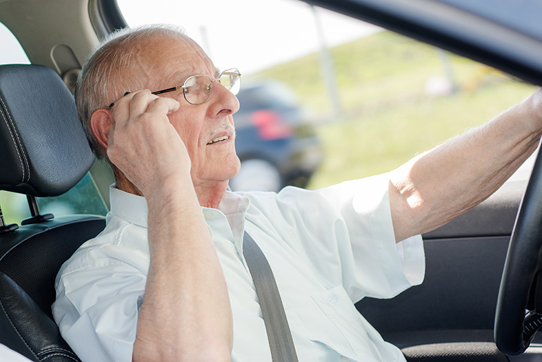 Older man driving and adjusting his hearing aid