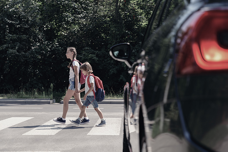 An older sister and younger brother crossing a Wisconsin street in front of a car