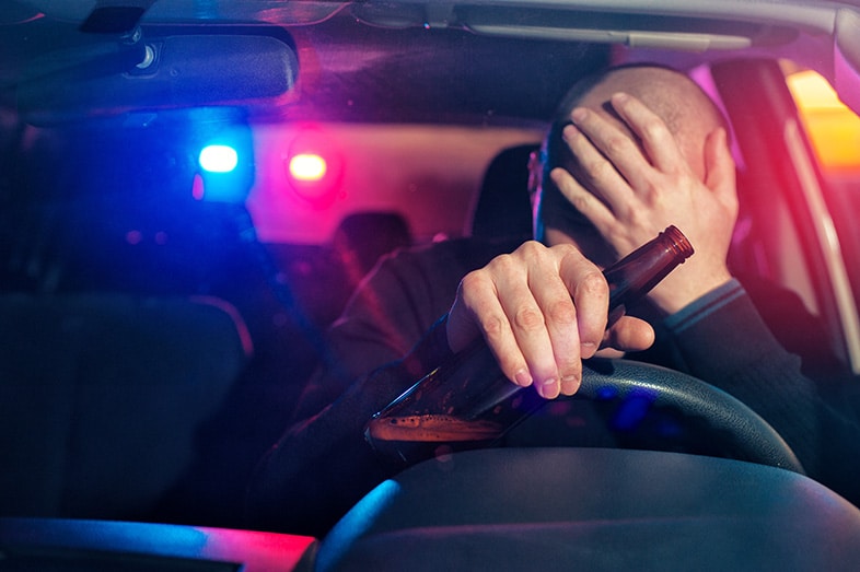 Drunk driver holding his head and a beer after getting pulled over by a police officer