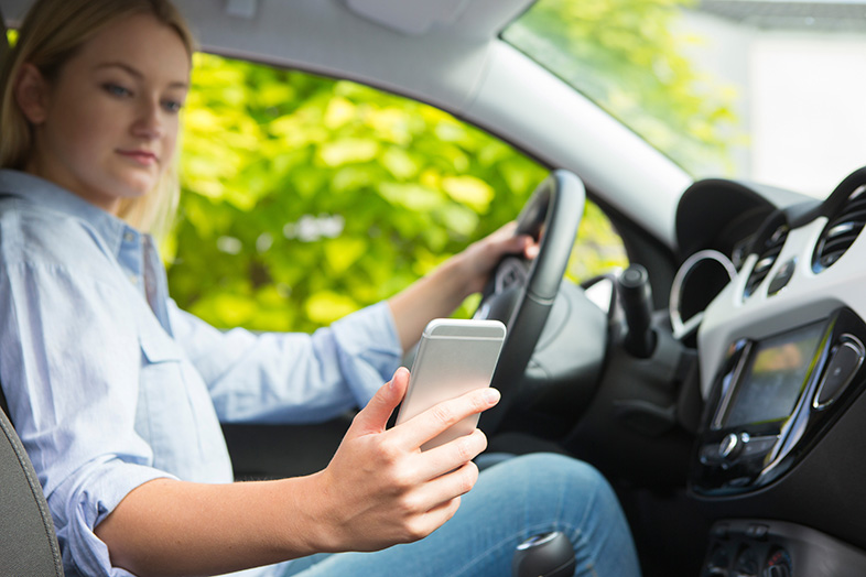Teenager looking at her phone while driving, increasing her risk of causing a crash