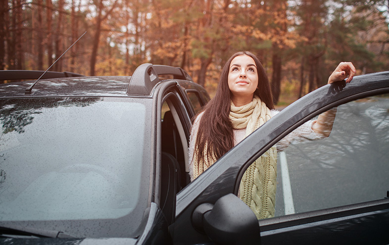 Woman standing outside her car admiring the autumn trees around her