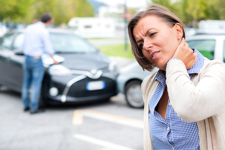 Woman holding her neck after a car accident, the other driver in the background looking at his phone