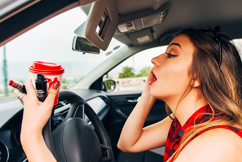 Distracted driver adjusting her makeup in the mirror and holding a coffee mug