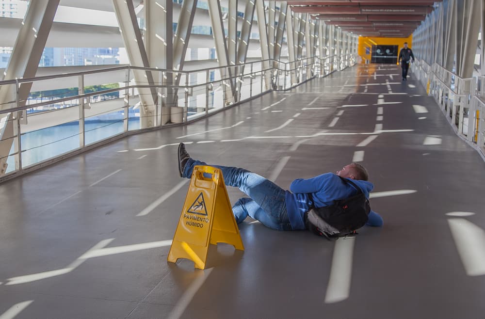 person fallen on the ground next to slippery floor sign