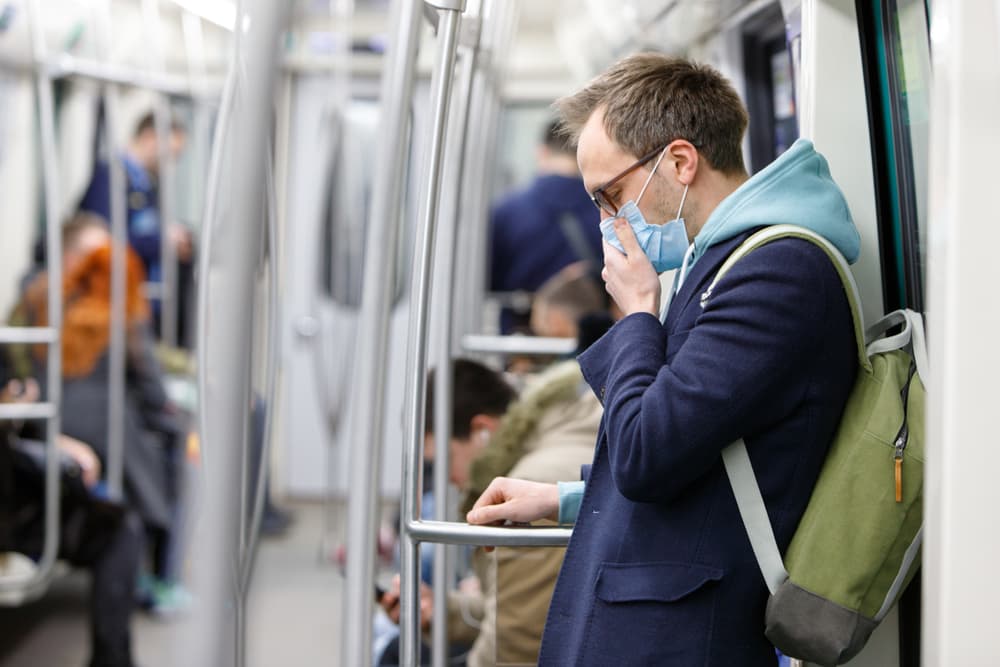 Sick man wearing glasses and protective mask, coughing in public transport for flu prevention and protection against infectious diseases.