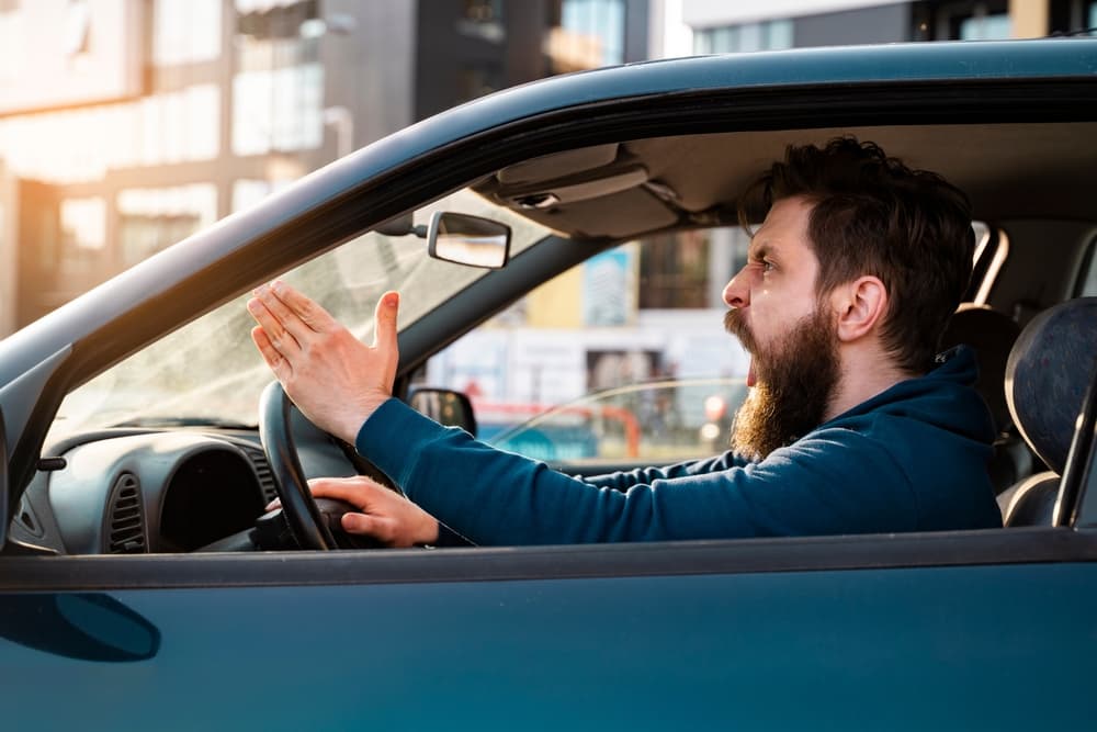 Frustrated bearded man expressing road rage, shouting in intense traffic situation - concept of aggressive behavior.