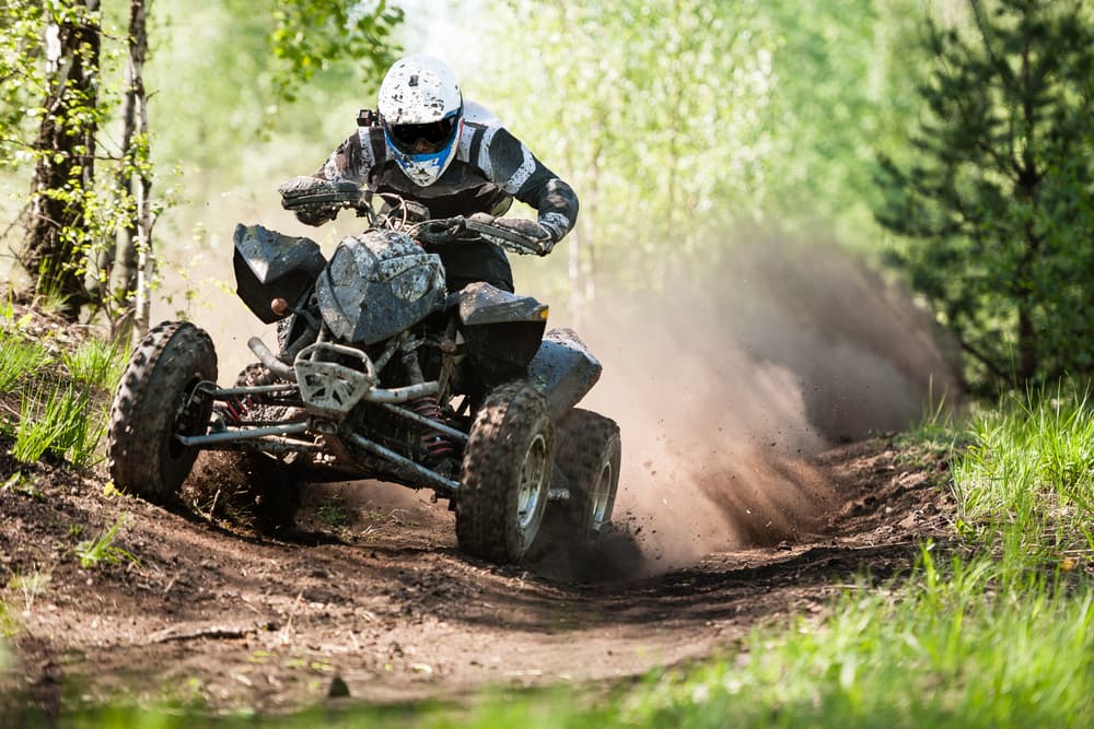 On a bright and sunny day, an ATV rider kicks up a substantial haze of dust and debris.