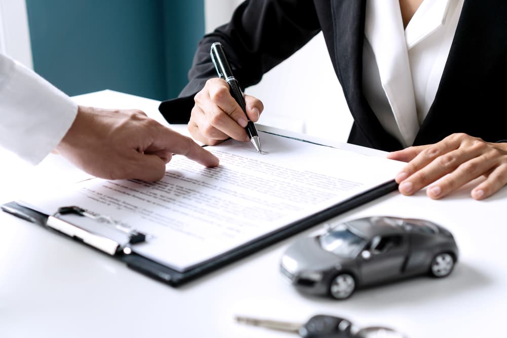 A close-up shot captures an Asian woman signing a car insurance document, lease paper contract, or agreement.