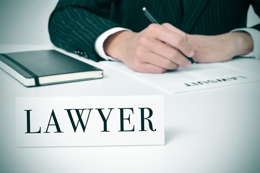 A man seated at his desk with a nameplate bearing the word "lawyer" in front of him.