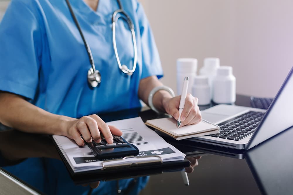 The concept of healthcare expenses and fees is illustrated as a smart doctor utilizes a calculator, smartphone, and tablet to calculate medical costs at the hospital.