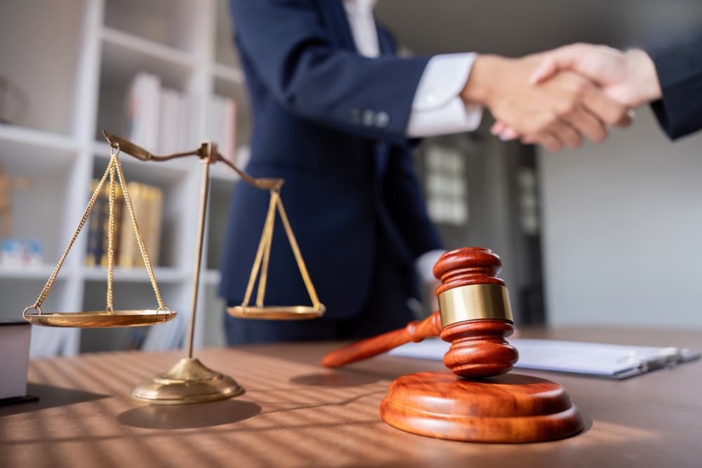 Professional Lawyer Handshake in Business Meeting with Scales of Justice and Gavel on Desk, Symbolizing Legal Agreement and Partnership in Modern Office Setting