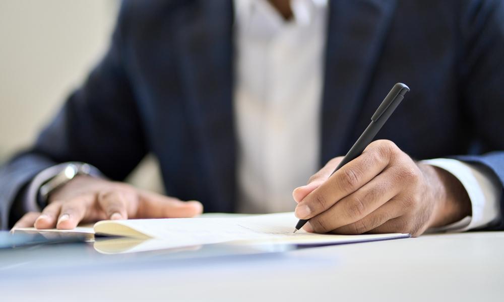 Business professional signing legal documents at office desk during meeting.