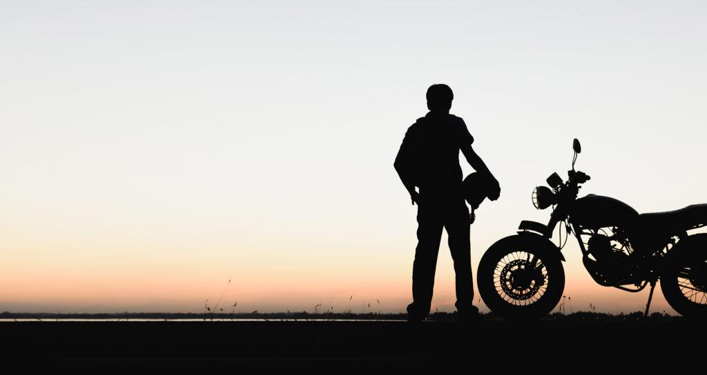 Rider stands next to motorcycle at sunset