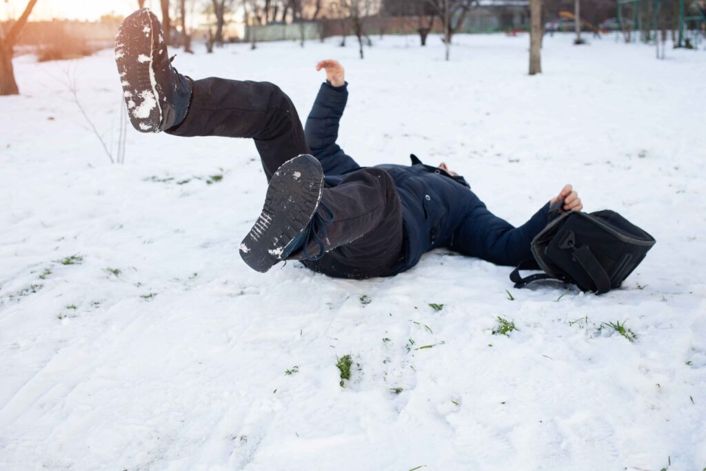 Person slipping and falling on icy snow-covered ground during winter.