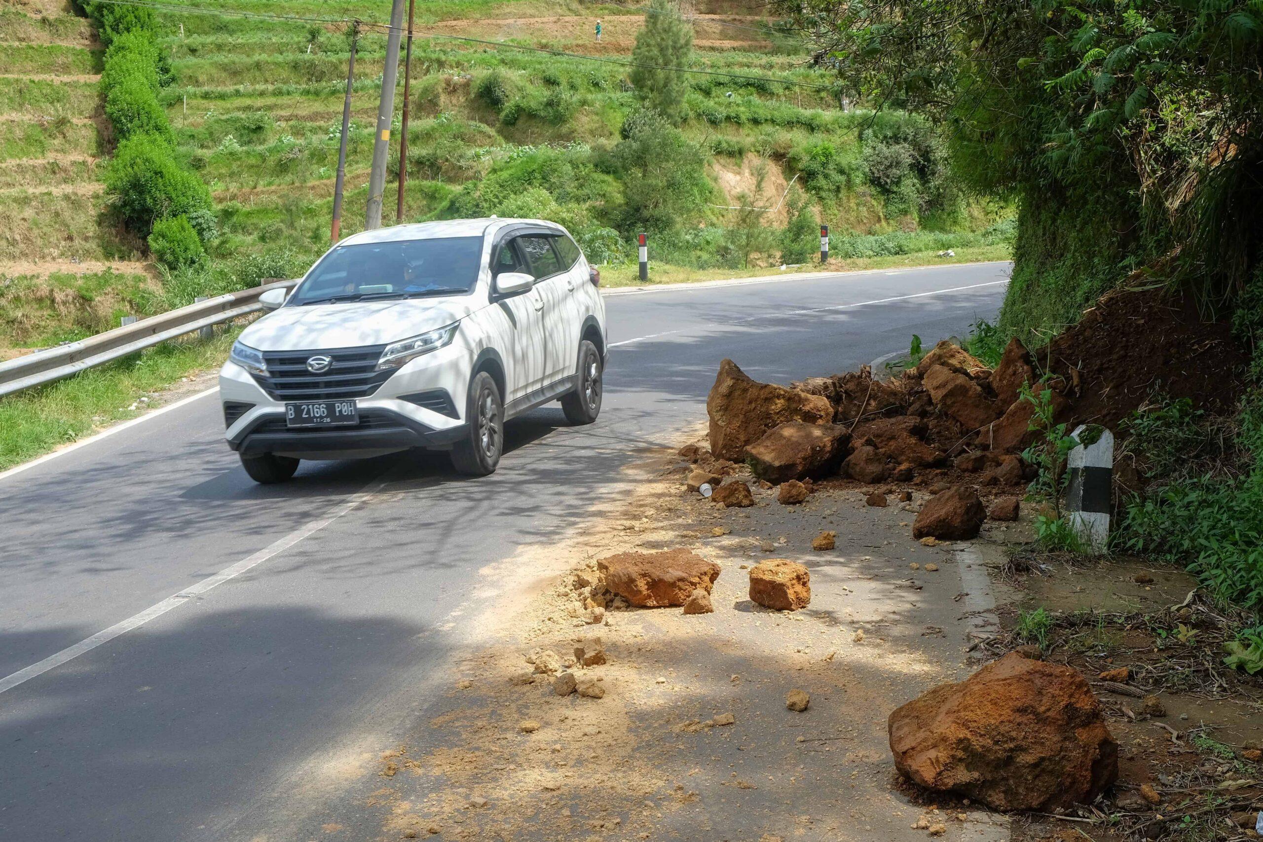 Car driving past fallen rocks from a landslide on a rural mountain road.