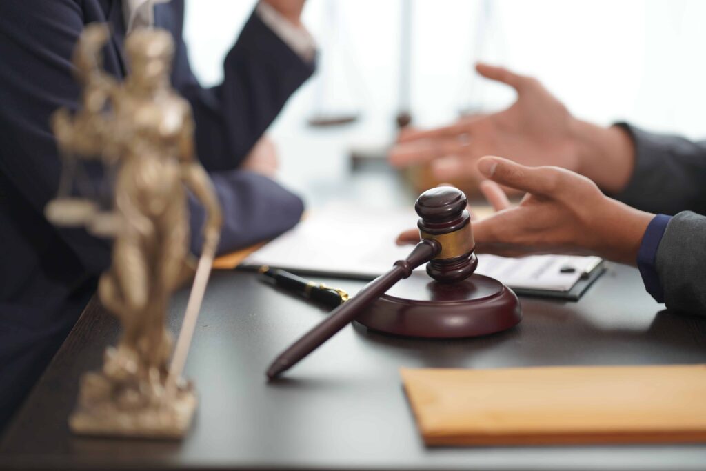 Lawyer and client discussing a legal case at a desk with a gavel and Lady Justice statue in the foreground.