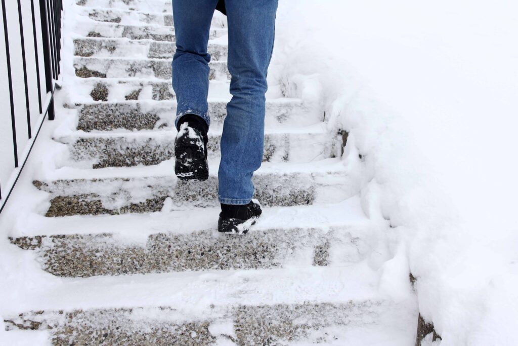 Person walking up snow-covered outdoor steps during winter, illustrating slippery conditions.