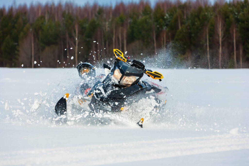 Snowmobile speeding through deep snow with rider in winter landscape, kicking up snow spray.