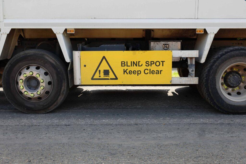 Blind spot warning sign on the side of a commercial truck reading ‘Blind Spot Keep Clear,’ highlighting truck blind spot safety