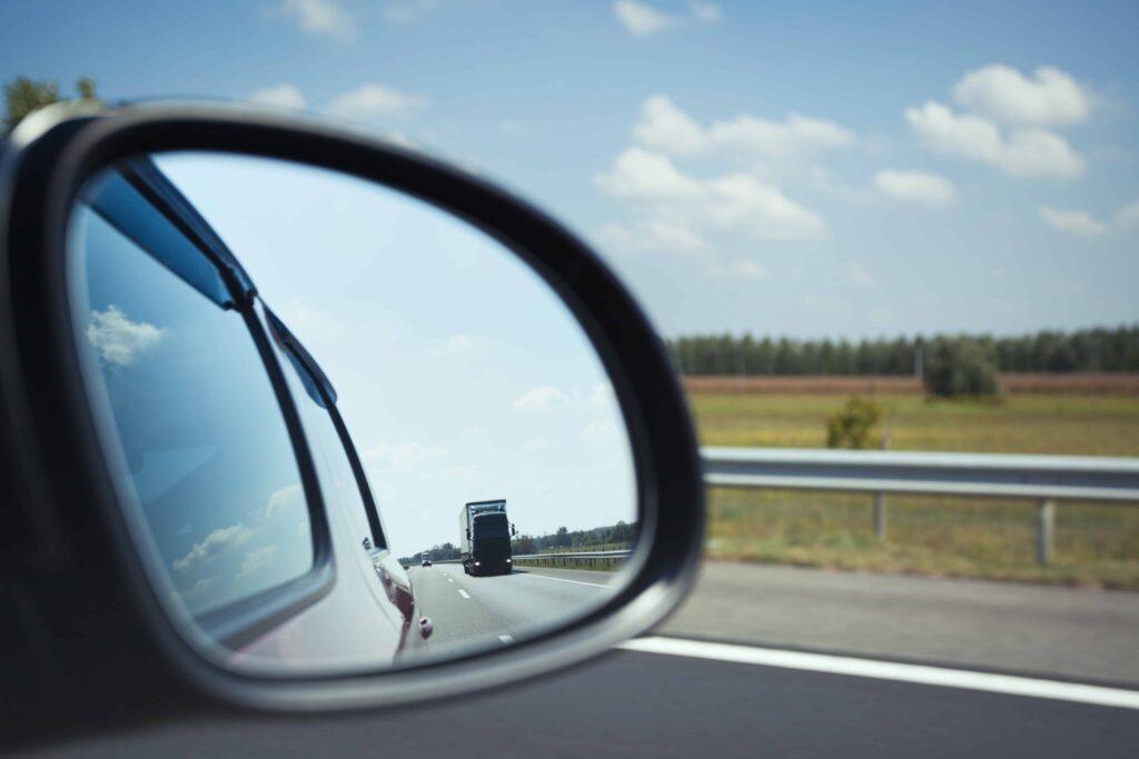 Truck visible in a car’s side mirror on a highway, illustrating commercial truck blind spots and driving safety risks