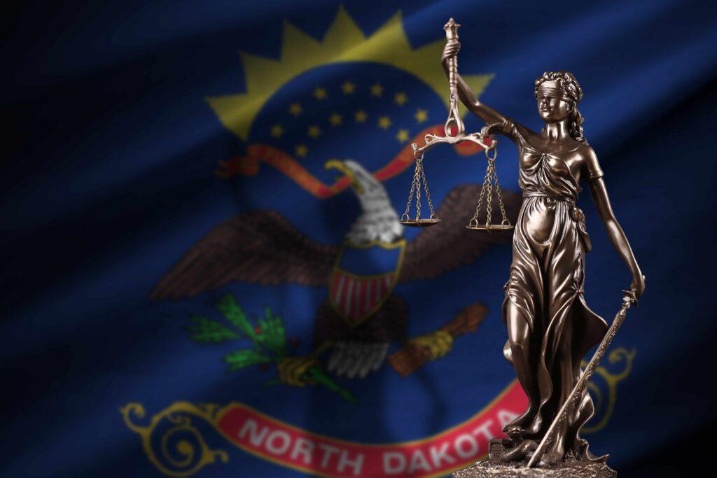 Lady Justice statue holding scales in front of the North Dakota state flag, symbolizing North Dakota courts and state legal system.