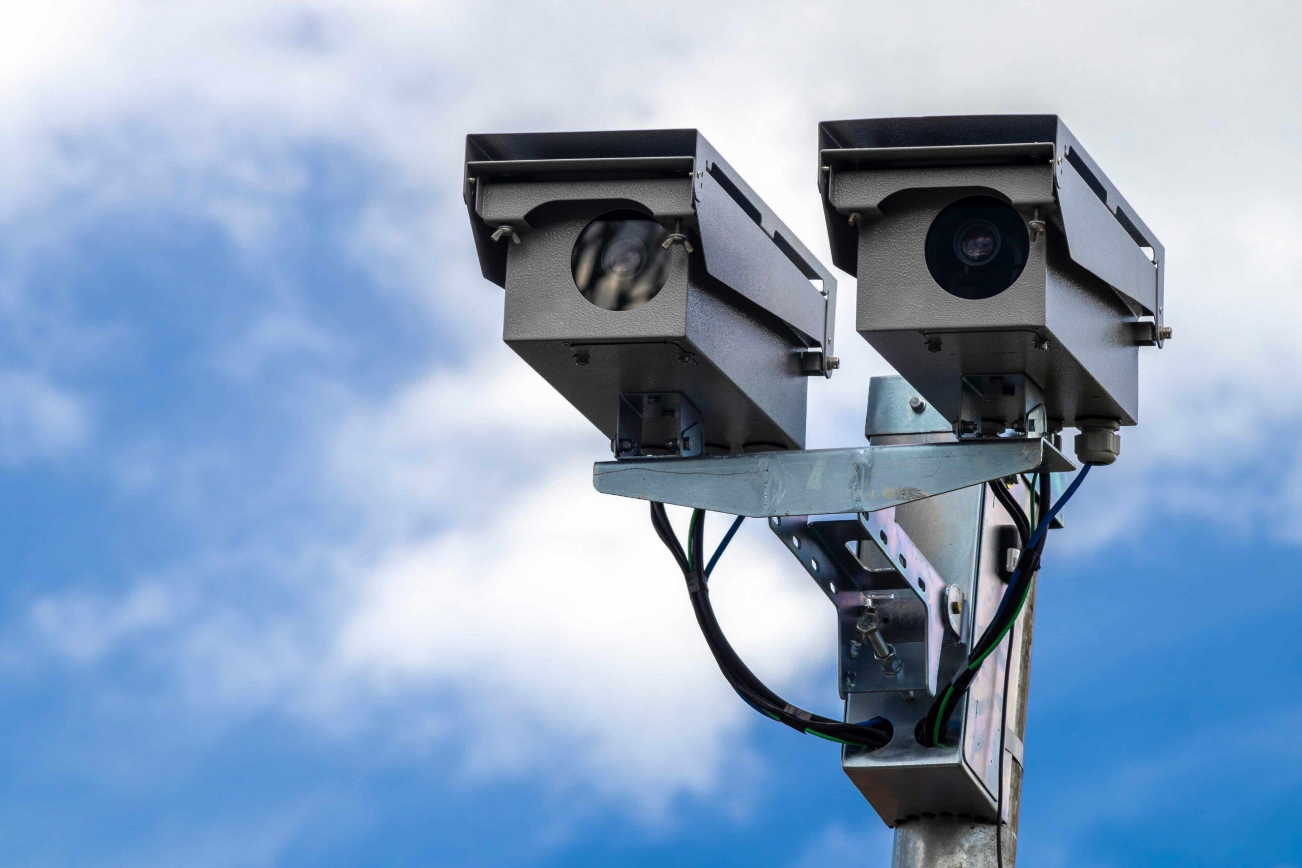 Traffic enforcement cameras mounted on a pole for speed monitoring and road safety surveillance against a blue sky