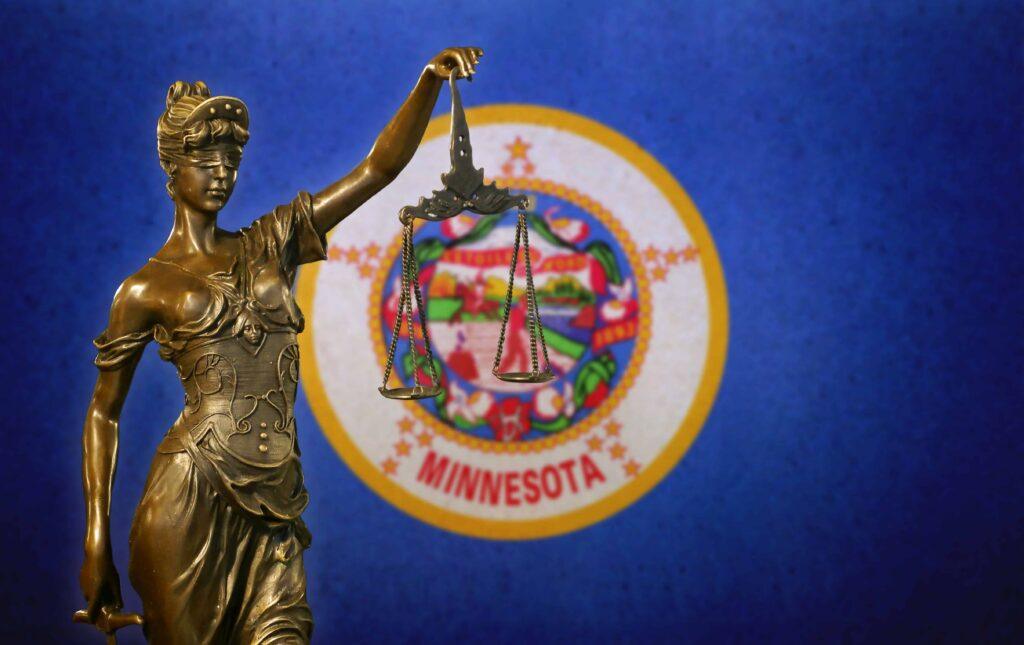 Statue of Lady Justice holding scales in front of the Minnesota state flag, symbolizing Minnesota courts and state law. Statue of Lady Justice holding scales in front of the Minnesota state flag, symbolizing Minnesota courts and state law.