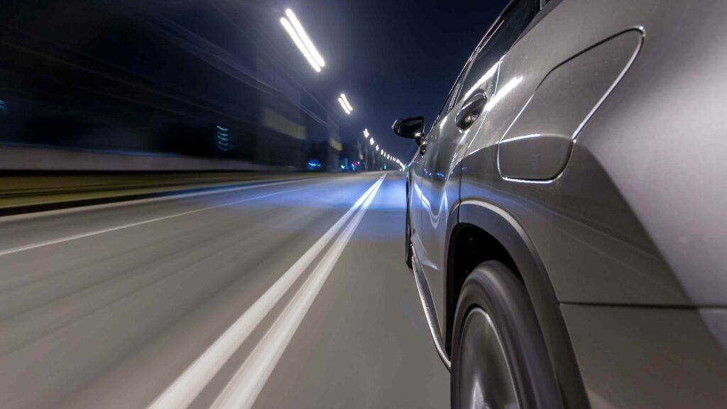 Car driving at high speed on a highway at night with motion blur and illuminated road lights, representing fast travel and road safety.