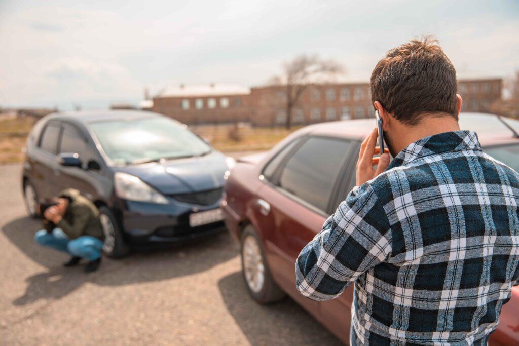 Driver calling emergency services after car accident, with injured person near damaged vehicle, illustrating auto accident claim and personal injury situation.