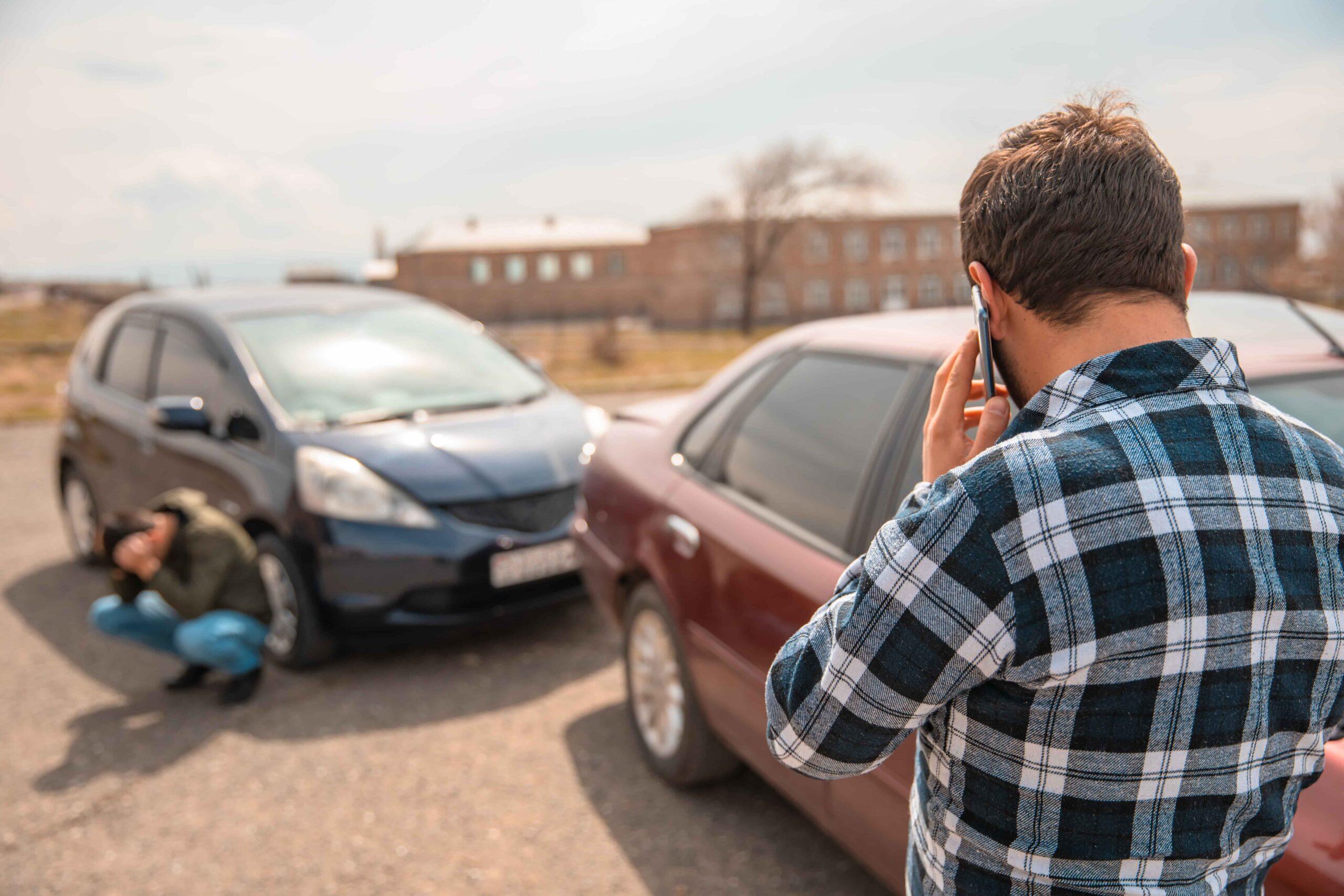 Driver calling emergency services after car accident, with injured person near damaged vehicle, illustrating auto accident claim and personal injury situation.