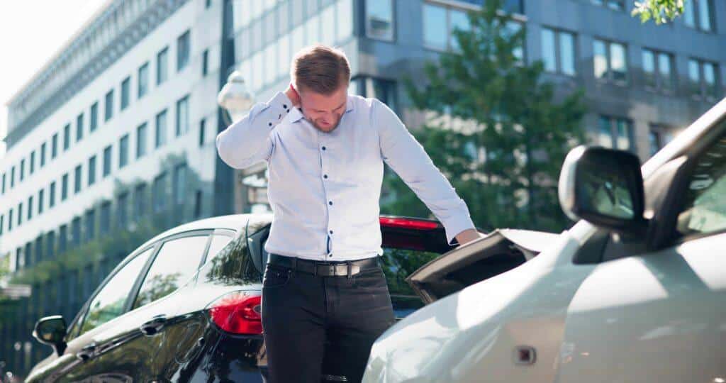 Man inspecting vehicle damage after car accident in city, highlighting auto collision, insurance claim, and personal injury situation.