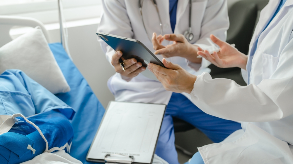A patient in hospital bed with wrapped arm, visited by two medical professionals