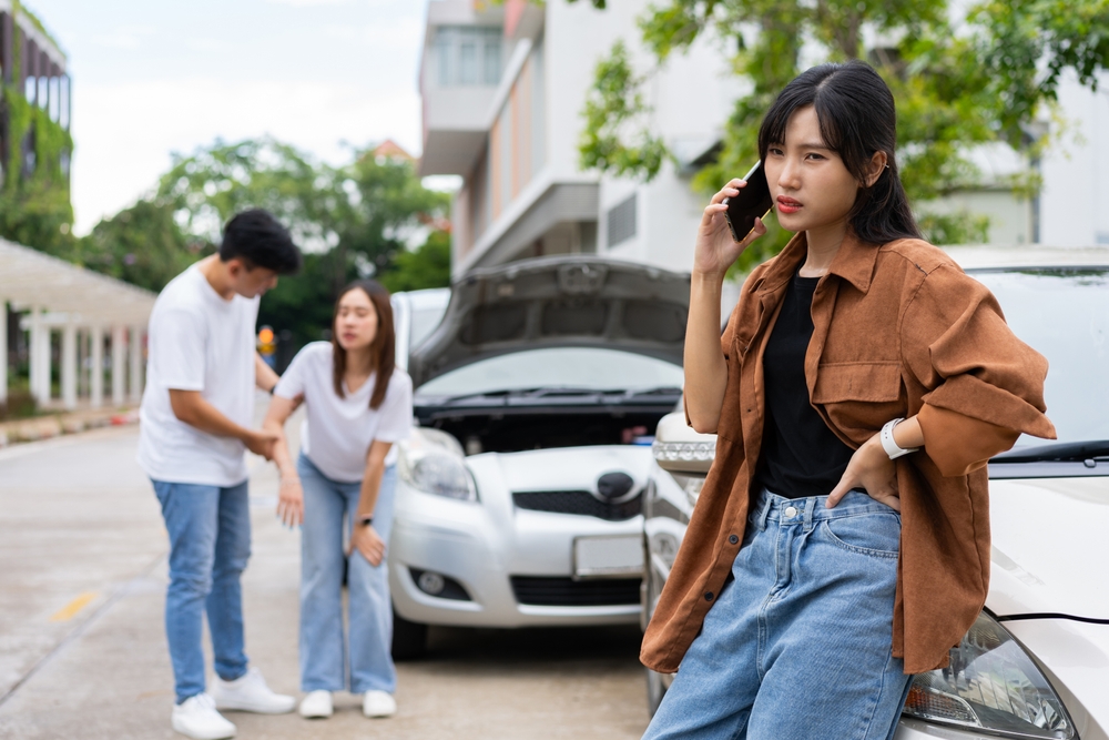 after a car accident, one driver calls for help while other tends to injured passenger in the background