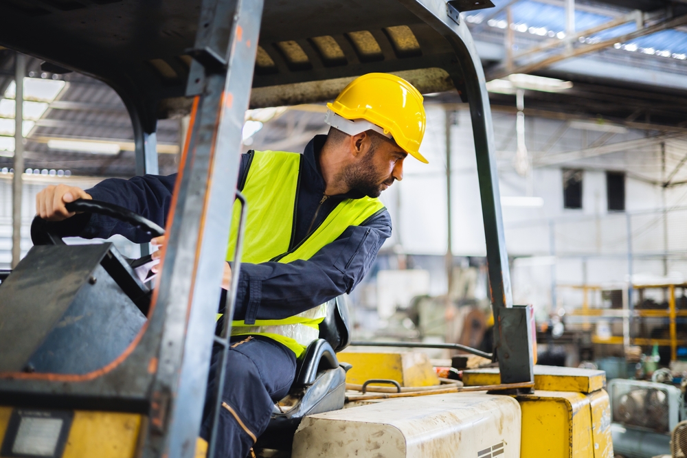 Worker in safety gear looking behind himself as he reverses a forklift