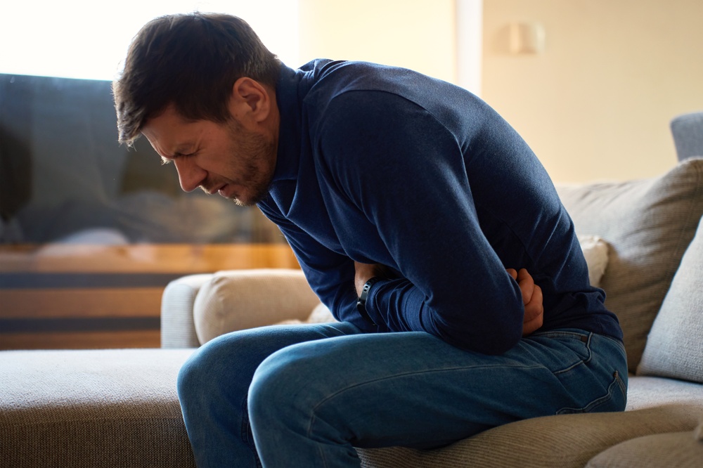 Man on couch, clutching his stomach in pain